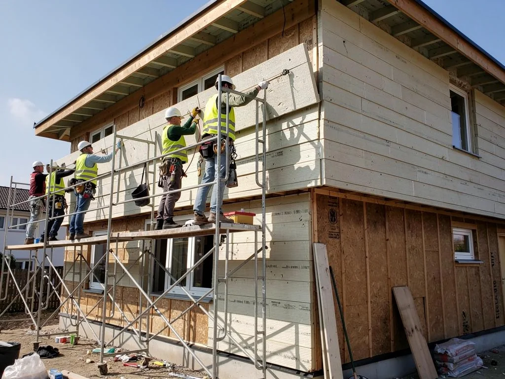 Ouvriers fixant des panneaux isolants sur un mur depuis l'échafaudage du chantier